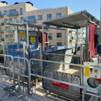 Bauaufzug transportiert Material, gesichert durch Geländer und Bedienelemente, vor einem modernen Wohngebäude.