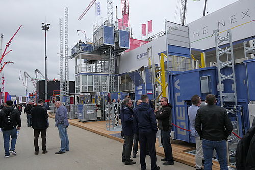 Menschen stehen und unterhalten sich vor großen Baumaschinen und Ausstellungskonstruktionen auf einer Messe im Freien.