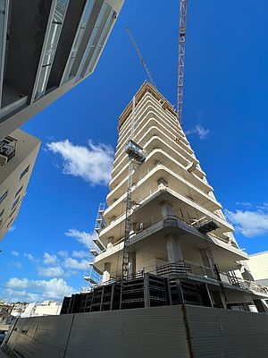 Ein unvollendetes Hochhaus ragt in den blauen Himmel, während ein Baukran darüber schwebt.