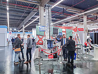 Eine Gruppe von Personen steht auf einer Messe neben einem Ausstellungsstand mit Tafel „GEDA Industriebühne X“.
