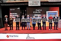 Personengruppe hält gerahmte Zertifikate und stehen nebeneinander auf rotem Teppich.