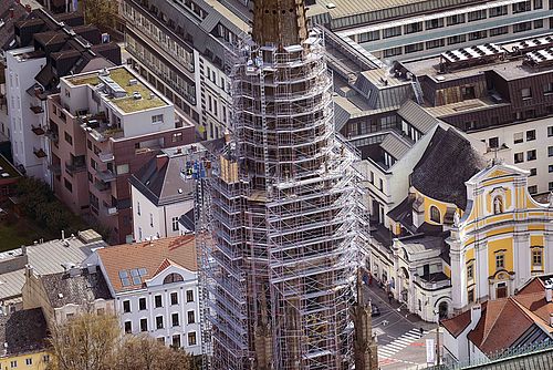 Ein Kirchturm wird von Baugerüsten umgeben und Arbeiter sind daran tätig.
