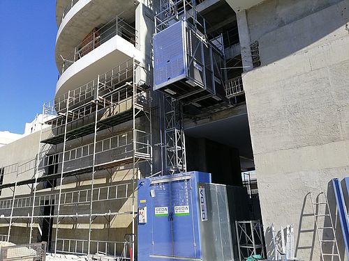 Ein Baustellenaufzug hebt Baumaterialien an einer Baustelle hoch.