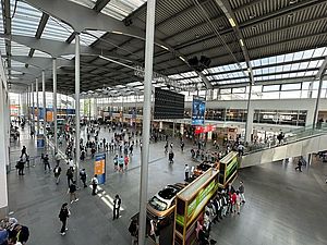 Menschen gehen in einer geräumigen Bahnhofshalle.