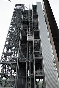 Ein hoher, grauer Industriebau mit zahlreichen stählernen Streben steigt in den Himmel mit einem Bauaufzug.
