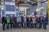 Eine Gruppe von Männern steht in einer Fabrikhalle vor Maschinen mit der Aufschrift "GEDA".