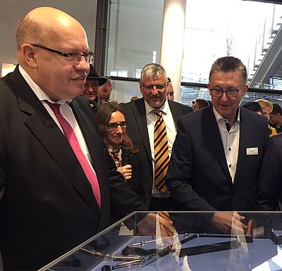 Peter Altmaier steht mit anderen Personen um eine Glasvitrine.