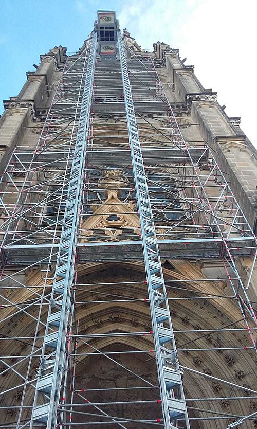 Gerüst ragt an hoher gotischer Kathedrale in die Höhe, umgeben von verzierten Fassadendetails.