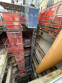 Bauaufzug transportiert Material entlang eines hohen Gestells in einer Baustelle.