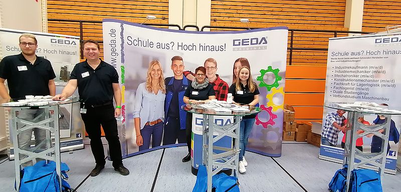 Personengruppe steht an einem Messestand mit Bannern und Informationsmaterialien.
