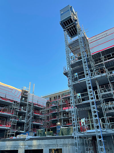 Baugerüst erhebt sich über mehrstöckiges Gebäude, auf dem eine Baustelle mit mehreren Etagen, Gerüsten und Aufzügen sichtbar ist.