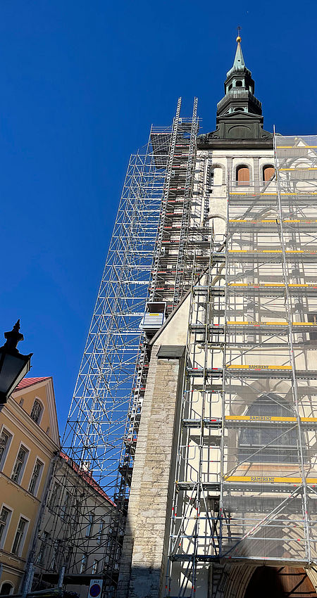 Gerüst umgibt einen Kirchturm, der renoviert wird vor blauem Himmel.