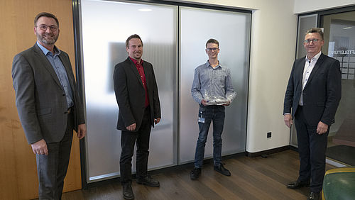 Vier Männer stehen nebeneinander lächelnd in einem Büro.