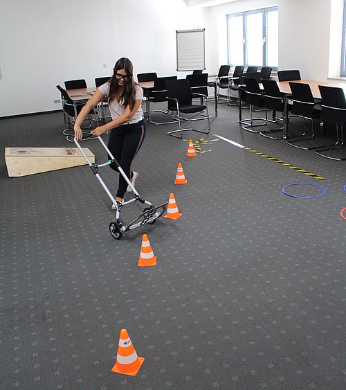 Eine Frau fährt einen Schiebewagen durch einen Parcours aus orangefarbenen Hütchen.