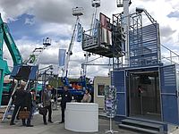 Baugerüst-Anlage wird von mehreren Personen betrachtet; sie unterhalten sich neben einem weißen Stehtisch.