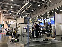 Eine Maschine führt Abfüllprozesse in einer Messehalle durch, umgeben von technischen Ausstellungsstücken und Besuchern.