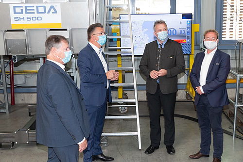 Vier Männer mit Masken stehen im Gespräch in einer Fabrikhalle.