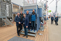 Fünf Männer stehen auf einer Plattform eines Industrielift-Containers namens GEDA und lächeln.