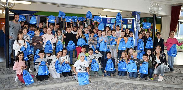 Eine Gruppe von Kindern halten blaue Taschen hoch.