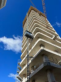 Ein unvollendetes Hochhaus ragt in den blauen Himmel, während ein Baukran darüber schwebt.