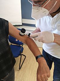 Eine Person untersucht mit einem Dermatoskop den Arm einer anderen Person.