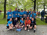 Eine Gruppe von Personen in blauen Sporttrikots posiert lächelnd auf einem gepflasterten Weg, umgeben von Bäumen.